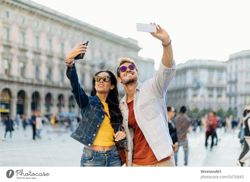 Happy young couple taking selfies in the city, Milan, Italy touristic tourists telecommunication phones telephone telephones cell phone cell phones Cellphone