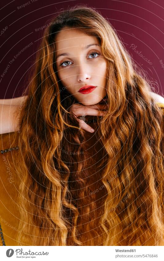 Portrait of young woman with long brown wavy hair leaning on chair against colored background color image colour image beautiful Woman beautiful Women people