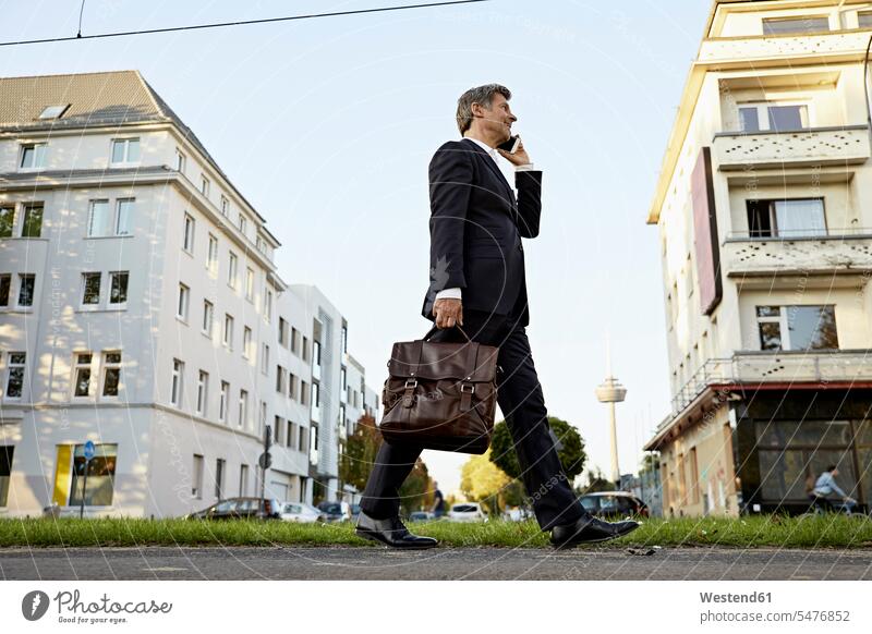 Mature businessman walking and using smartphone in the city Businessman Business man Businessmen Business men going town cities towns Smartphone iPhone