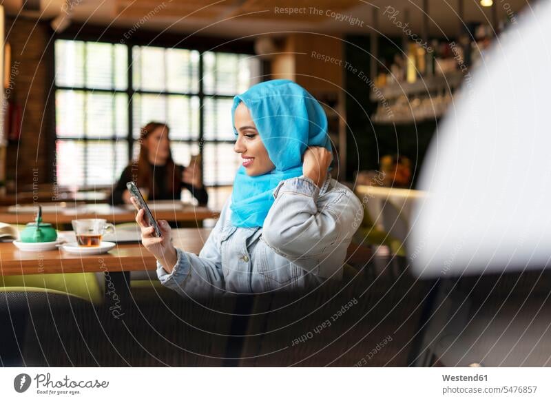 Young woman wearing turquoise hijab and using smartphone in a cafe human human being human beings humans person persons caucasian appearance caucasian ethnicity