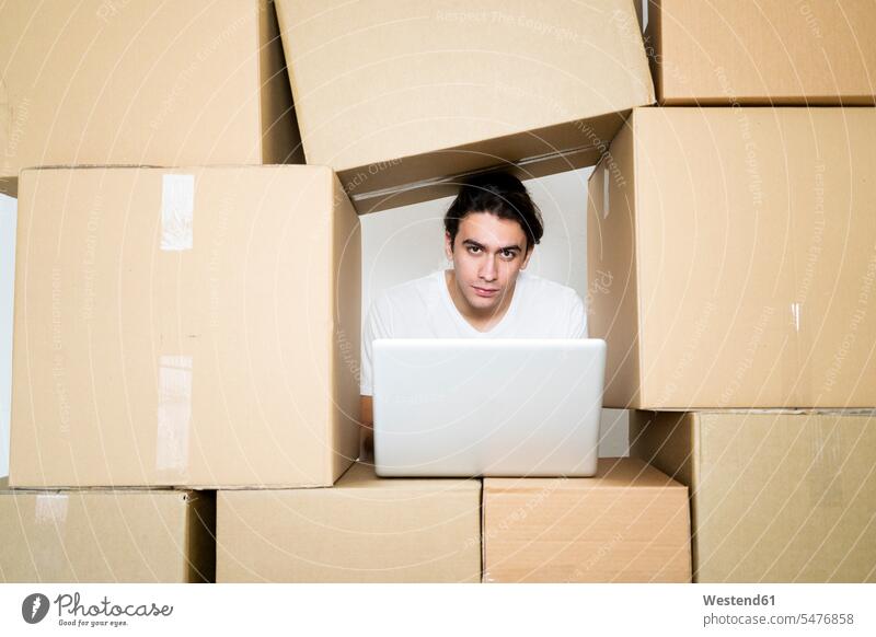 Young man with laptop while trapped between cardboard boxes at new apartment color image colour image indoors indoor shot indoor shots interior interior view