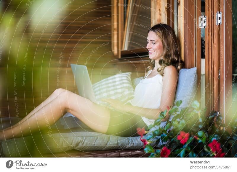 Smiling woman on balcony using laptop relaxed relaxation balconies females women smiling smile Laptop Computers laptops notebook relaxing Adults grown-ups