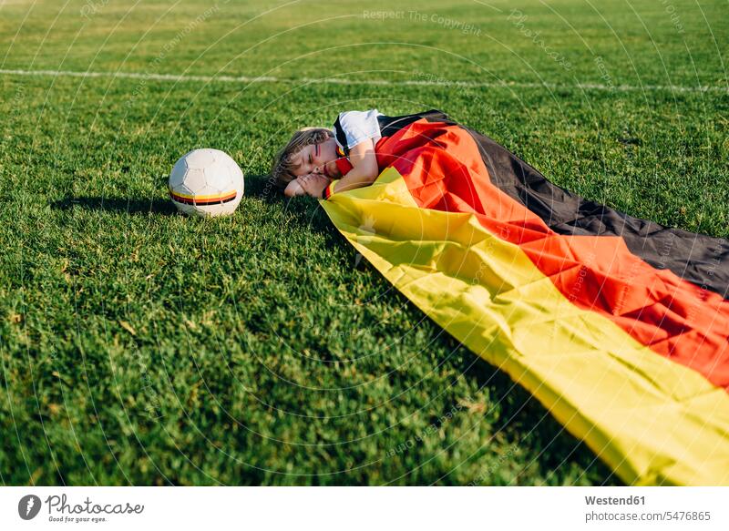 Boy sleeping on soccer field, covered iwith German flag football shirt football shirts soccer jerseys boy boys males asleep balls lying laying down lie