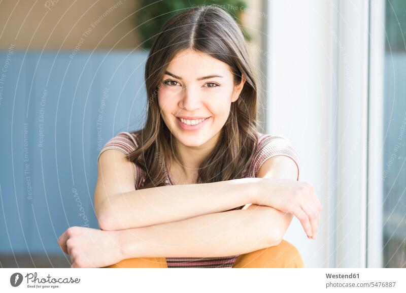 Portrait of smiling young woman sitting at the window at home females women Seated smile portrait portraits windows Adults grown-ups grownups adult people