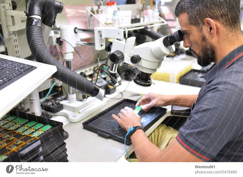 Man using a microscope for the quality control in the manufacturing of circuit boards for the electronics industry Quality check Quality test factory factories