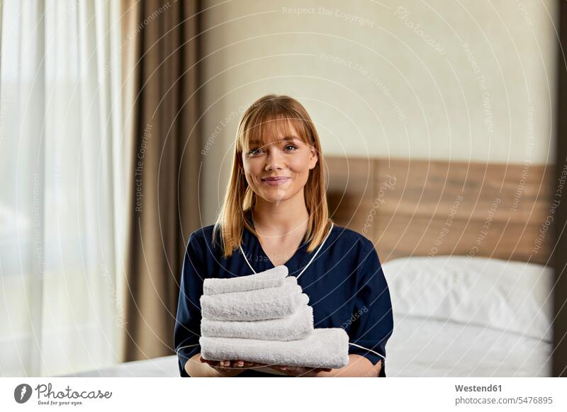 Smiling chambermaid holding towels while standing in hotel bedroom color image colour image indoors indoor shot indoor shots interior interior view Interiors