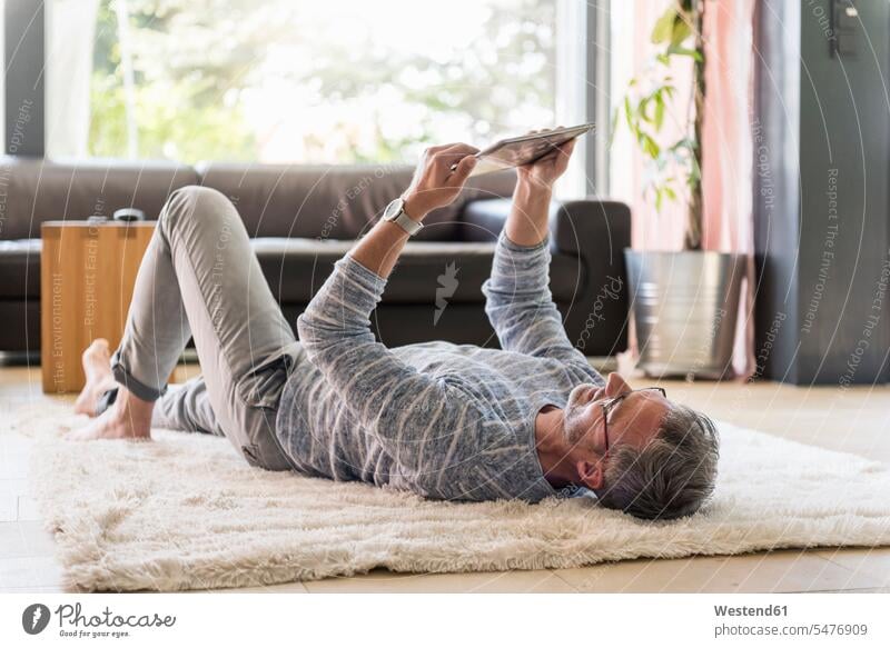 Mature man lying on carpet at home using a tablet carpets rug rugs laying down lie lying down men males digitizer Tablet Computer Tablet PC Tablet Computers