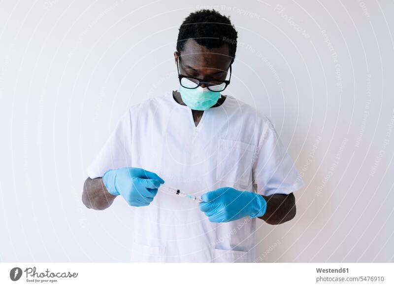 Afro doctor holding syringe and vial while standing against white background color image colour image Spain white backdrop plain background cut out cutout