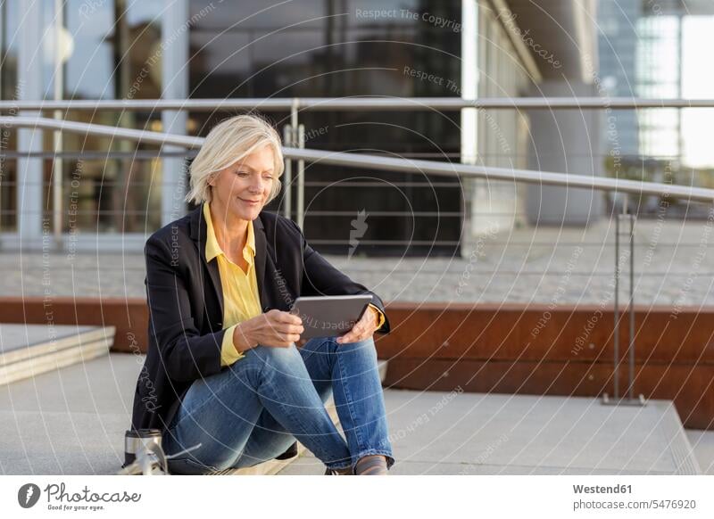 Smiling senior businesswoman sitting with tablet in the city confidence confident Seated smiling smile businesswomen business woman business women digitizer