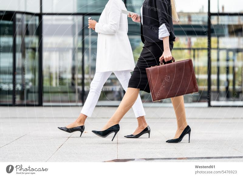 Businesswoman with briefcase using mobile phone while walking by colleague on footpath color image colour image outdoors location shots outdoor shot