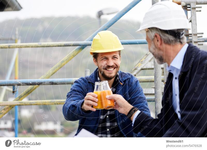Happy architect and worker on scaffolding on a construction site clinking juice bottles Occupation Work job jobs profession professional occupation blue collar
