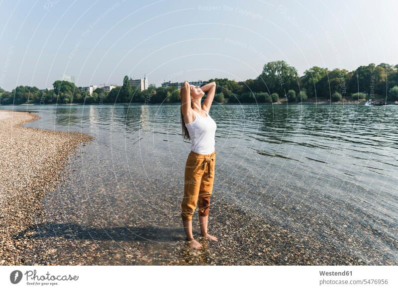 Happy young woman standing relaxed in water of a river relaxation riverside riverbank happiness happy River Rivers females women relaxing water's edge waterside