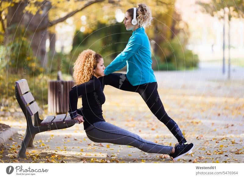 Two sportive young women stretching in park sporting sporty athletic female friends parks woman females sports mate friendship Adults grown-ups grownups adult