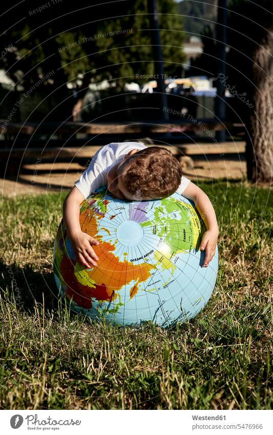 Boy embracing globe on grassy land in park during sunny day color image colour image Spain leisure activity leisure activities free time leisure time
