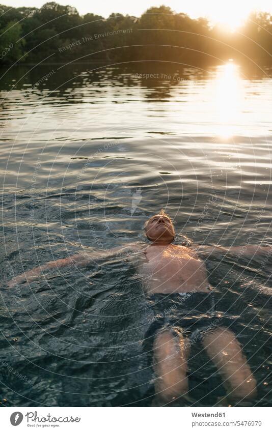 Senior man swimming in a lake at sunset lakes sunsets sundown men males senior men senior man elder man elder men senior citizen water waters body of water
