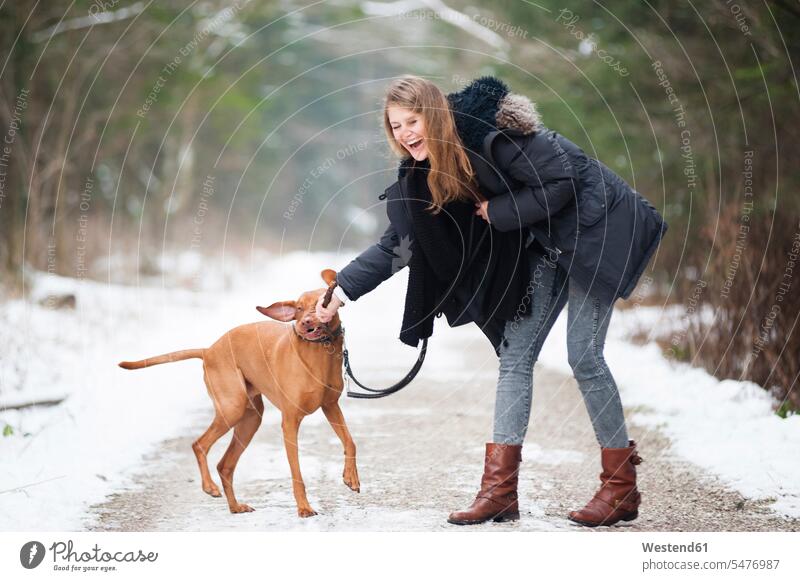 Cheerful young woman playing with dog on road in forest during winter color image colour image leisure activity leisure activities free time leisure time