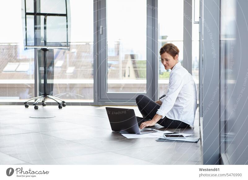 Businesswoman sitting on the floor in office using laptop Seated businesswoman businesswomen business woman business women offices office room office rooms