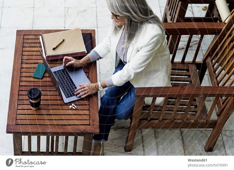 Female entrepreneur using laptop while sitting at wooden table in garden color image colour image Spain outdoors location shots outdoor shot outdoor shots day