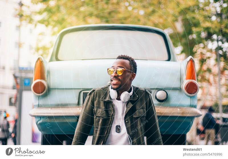 Young man wearing sunglasses sitting against vintage car in city color image colour image Spain leisure activity leisure activities free time leisure time