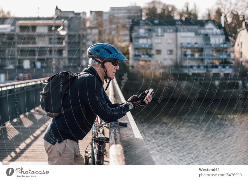 Senior man with cyclist helmet using smartphone on bridge riding bicycle riding bike bike riding cycling bicycling pedaling senior men senior man elder man