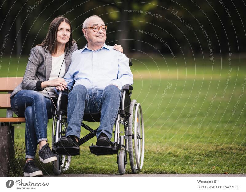 Portrait of senior man in a wheelchair relaxing with granddaughter in a park generation wheelchairs Seated sit Emotions Feeling Feelings Sentiment Sentiments