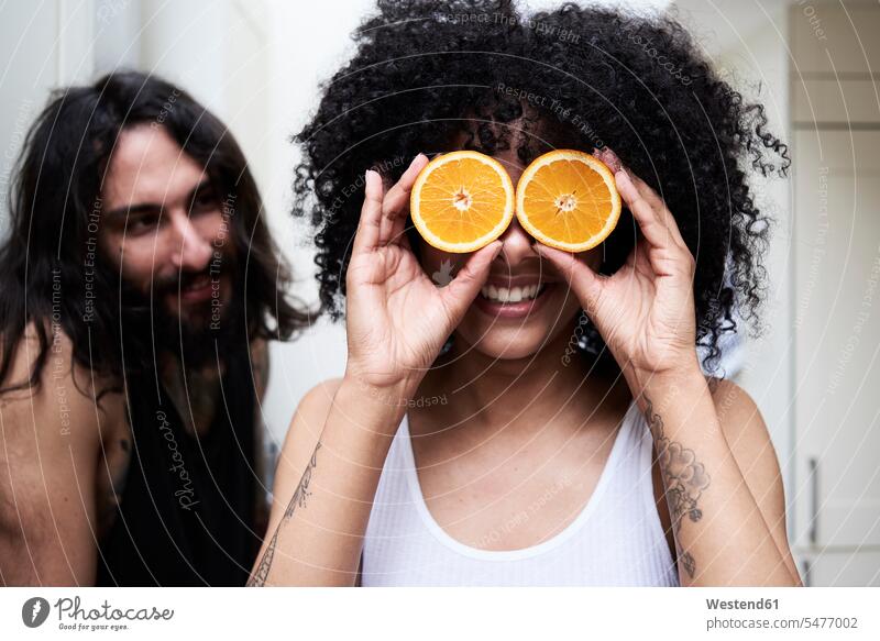 Happy young woman covering her eyes with oranges in kitchen couple twosomes partnership couples happiness happy healthy Orange Citrus sinensis Oranges playing