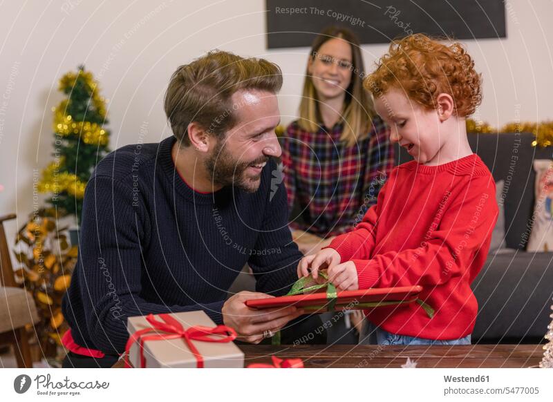 Smiling woman looking at father giving Christmas present to son in living room color image colour image leisure activity leisure activities free time