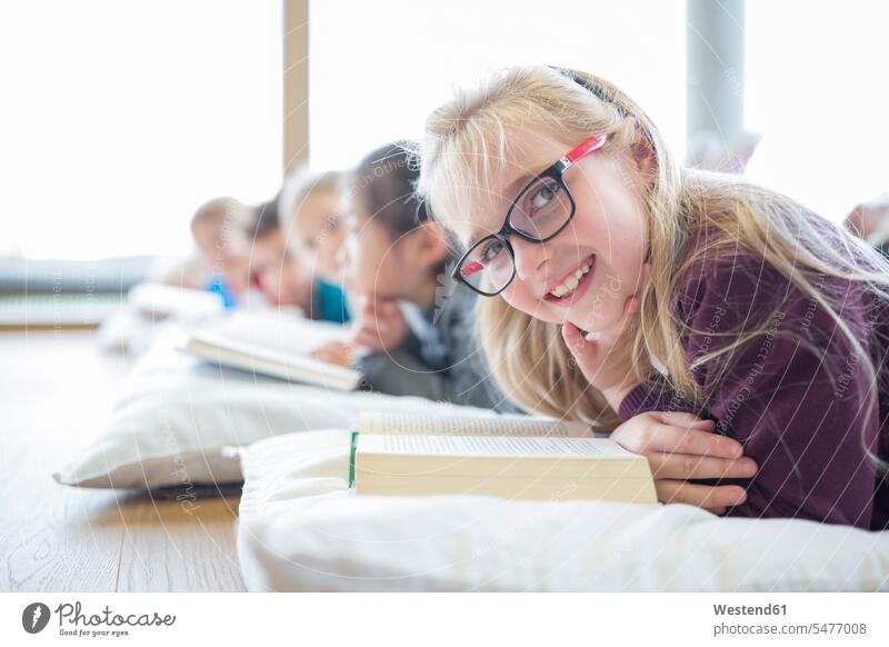 Portrait of smiling schoolgirl lying on the floor with classmates reading book in school break room books smile laying down lie lying down floors student pupils