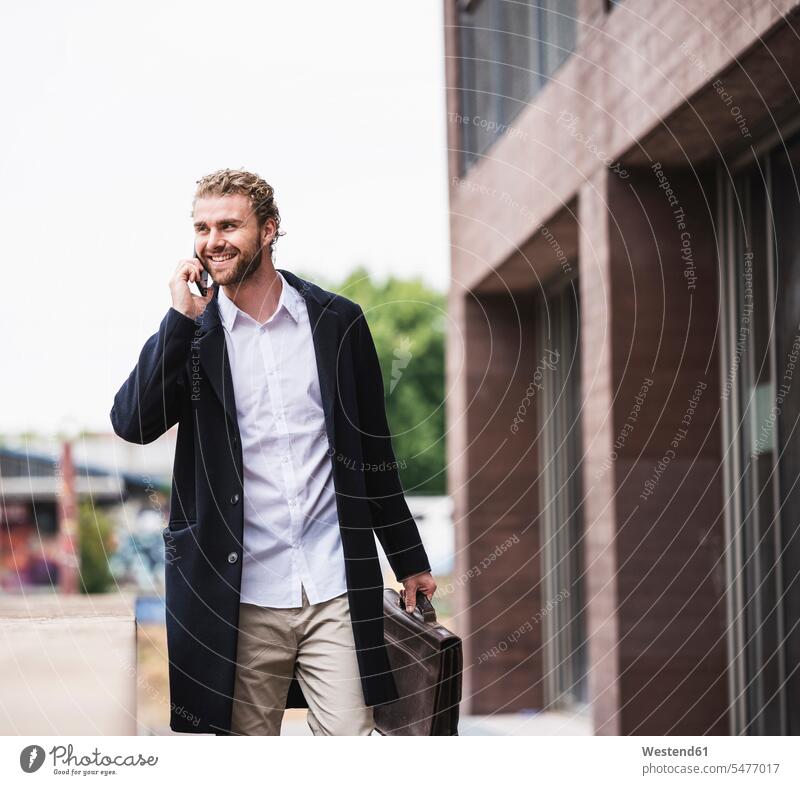 Smiling young businessman on cell phone outside office building office buildings on the phone call telephoning On The Telephone calling mobile phone mobiles