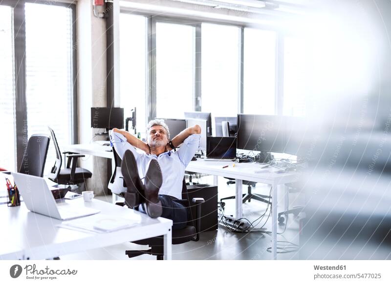 Relaxed mature businessman sitting at desk in office leaning back relaxed relaxation Seated Reclining Recline desks offices office room office rooms Businessman