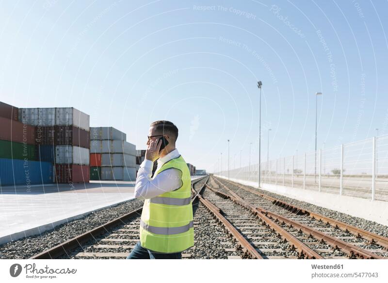 Man on railway tracks in front of cargo containers talking on cell phone Spain message exportation exporting import handling logistics company haulage company