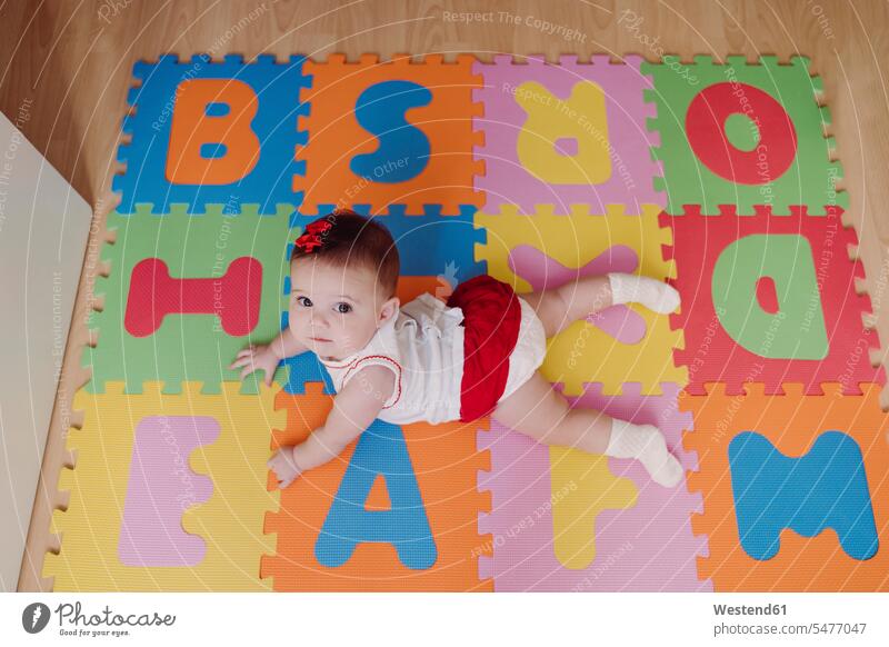 Cute baby girl lying on colorful puzzle playmat at home color image colour image Spain indoors indoor shot indoor shots interior interior view Interiors