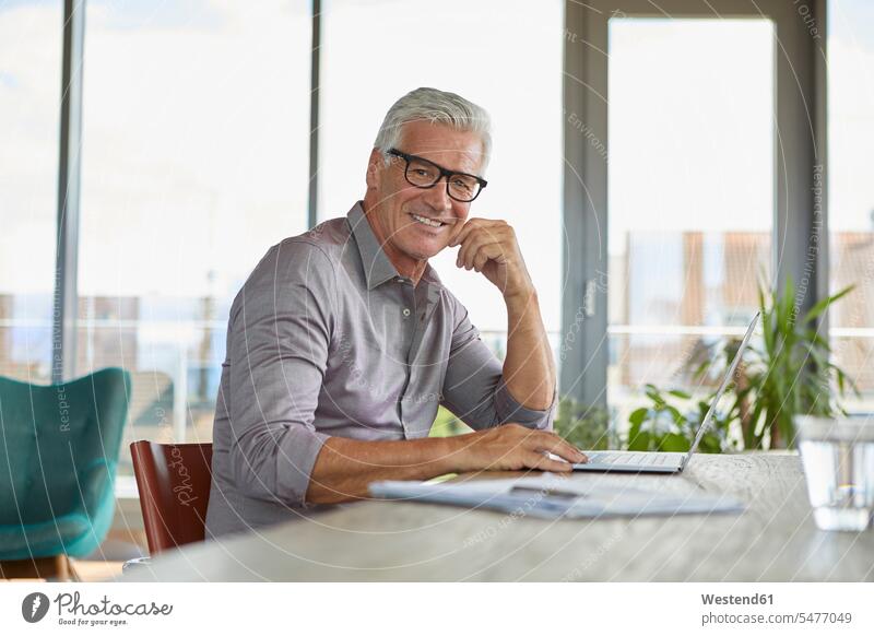 Portrait of smiling mature man using laptop on table at home smile Laptop Computers laptops notebook portrait portraits men males Table Tables computer