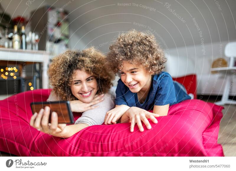 Mother and son watching a video on smartphone, lying on big pillow cushions telecommunication phones telephone telephones cell phone cell phones Cellphone