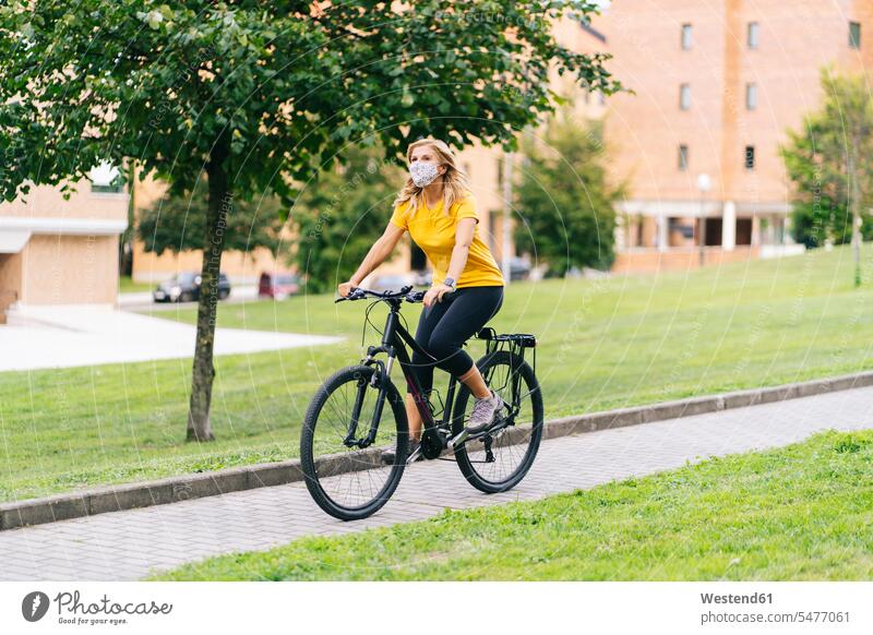 Woman wearing protective face mask cycling on footpath in city color image colour image outdoors location shots outdoor shot outdoor shots day daylight shot