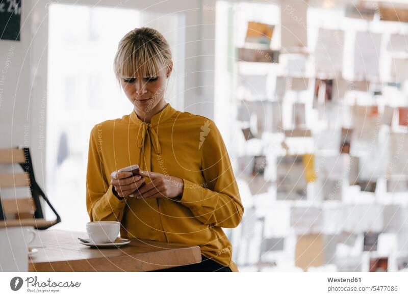 Blond businesswoman using smartphone in a coffee shop, reading text messages text messaging SMS Text Message Smartphone iPhone Smartphones portrait portraits