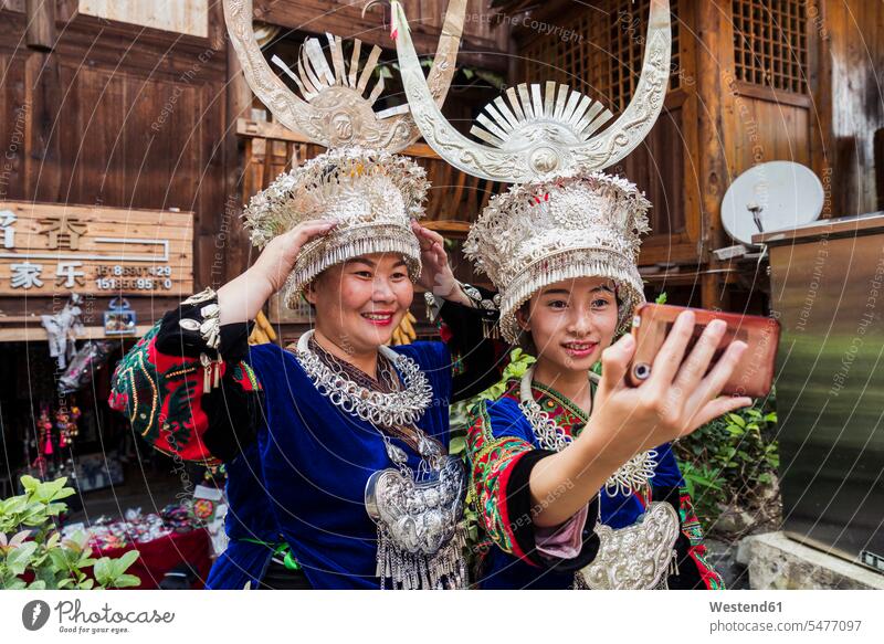 China, Guizhou, two Miao women wearing traditional dresses and headdresses taking a selfie with smartphone Mountain Village ritual rituals Smartphone iPhone