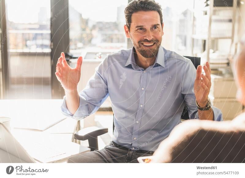 Smiling businessman having discussion with colleague while sitting at office color image colour image indoors indoor shot indoor shots interior interior view