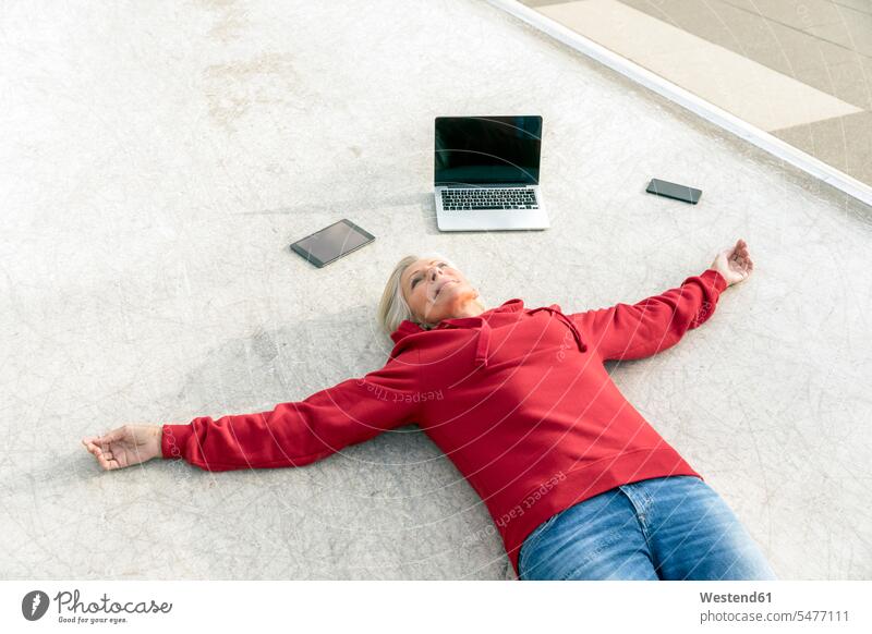 Senior woman wearing red hoodie lying on the ground next to mobile devices laying down lie lying down females women land floor Hoodie Hoody Adults grown-ups