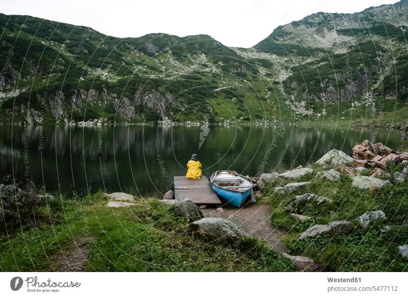 Austria, Tyrol, Fieberbrunn, Wildseeloder, woman sitting at the shore of lake Wildsee next to a boat Seated boats females women lakes vessel water vehicle