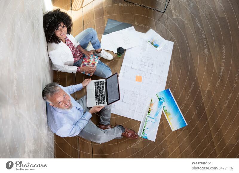 Businessman and businesswoman sitting on the floor in a loft working with laptop and documents Laptop Computers laptops notebook lofts Seated At Work