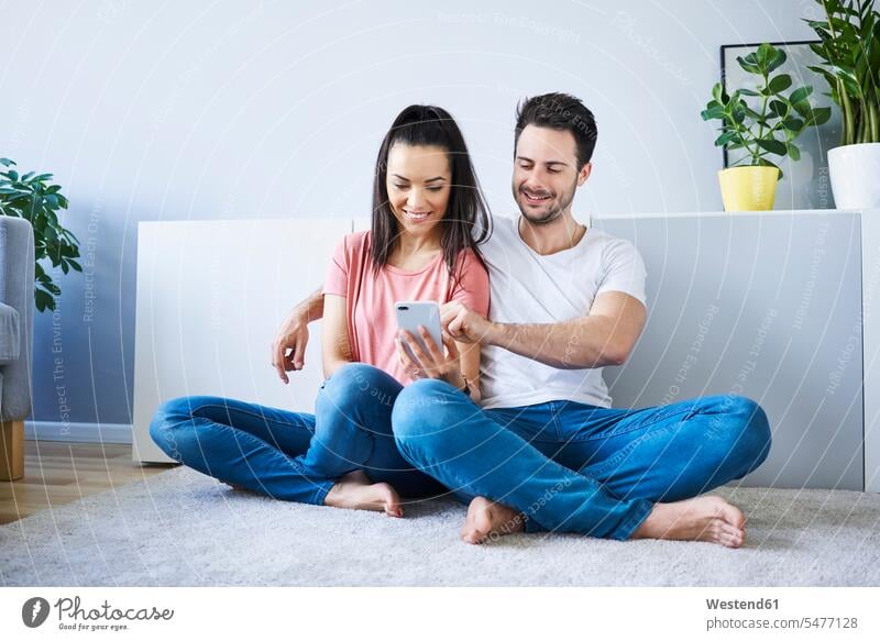 Couple sitting on floor and using smartphone Smartphone iPhone Smartphones Seated couple twosomes partnership couples floors mobile phone mobiles mobile phones