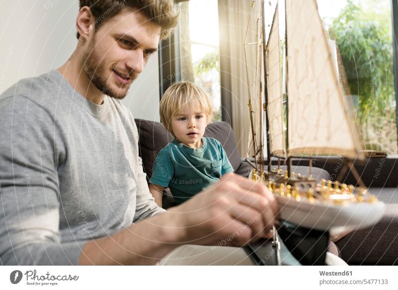Father and son looking at toy model ship on couch at home sitting Seated eyeing model boat settee sofa sofas couches settees father pa fathers daddy dads papa