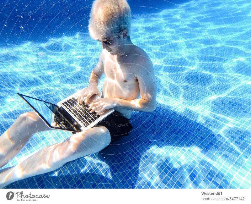 Shirtless young man wearing sunglasses using laptop underwater in swimming pool color image colour image Spain leisure activity leisure activities free time