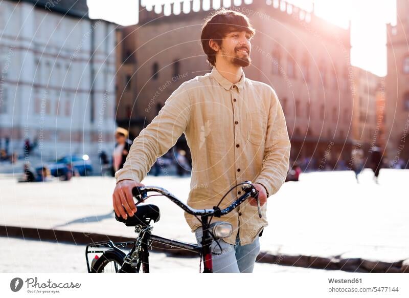 Italy, Bologna, portrait of relaxed young man pushing bicycle in the city men males portraits bikes bicycles town cities towns relaxation smiling smile Adults