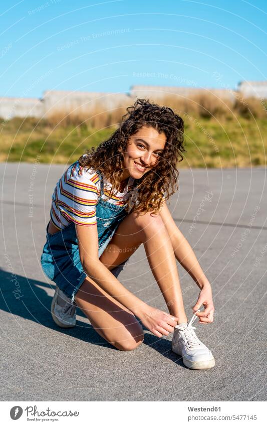 Young woman sitting on ground tying shoes smiling smile young women young woman Tying Shoelace tie shoe tie shoes Seated summer summer time summery summertime