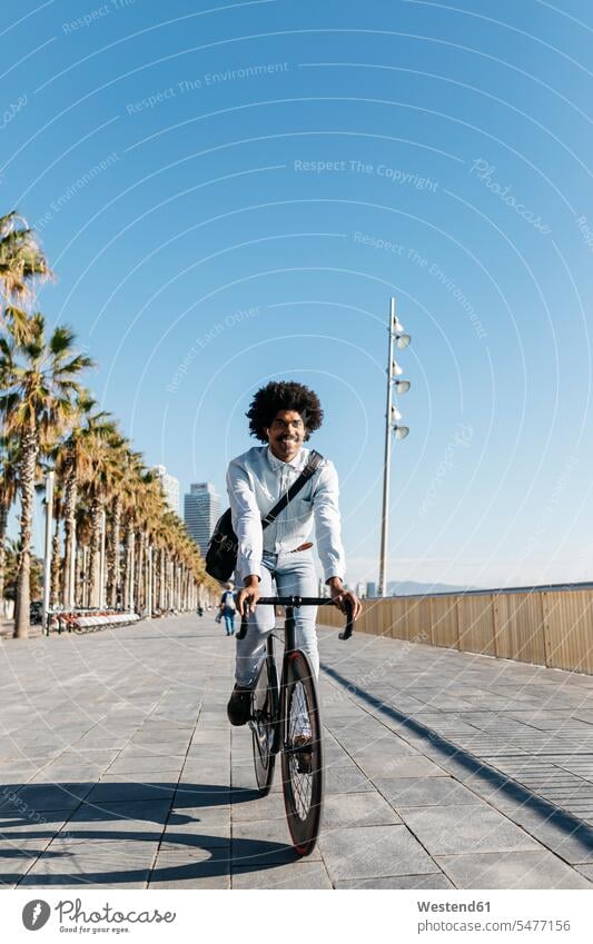 Mid adult man riding bicykle on a beach promenade, listening music bicycle bikes bicycles earphones ear phone ear phones sea front boardwalk Listening Music