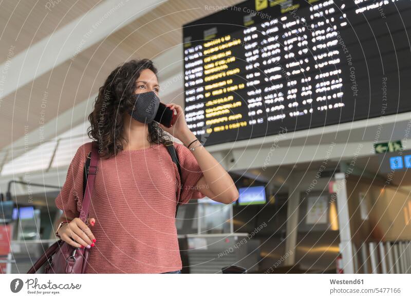 Young woman with protective face mask talking on smart phone while standing at airport color image colour image indoors indoor shot indoor shots interior