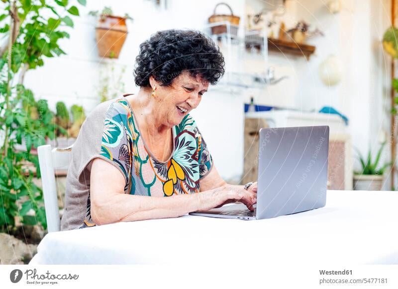 Happy senior woman using laptop on table while sitting in yard color image colour image Spain leisure activity leisure activities free time leisure time