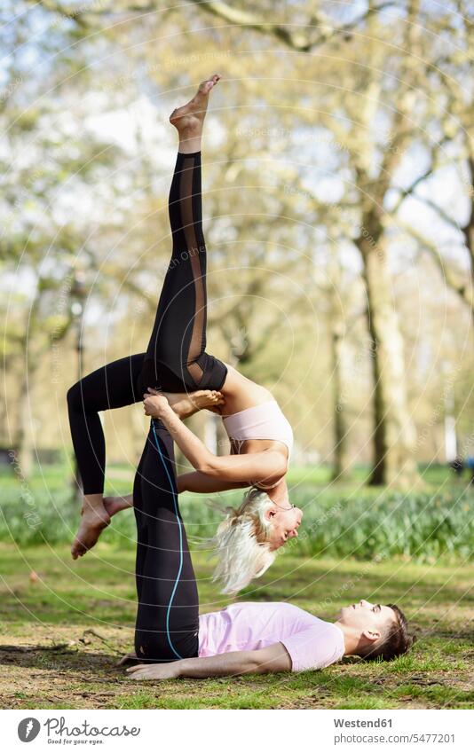 Young couple doing yoga acrobatics in an urban park England City Park municipal park workout working out work out exercise exercises sportive sporting sporty